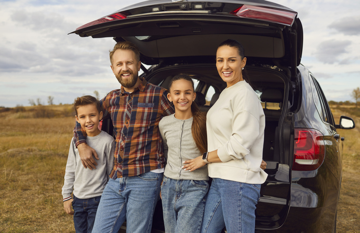 A family standing by their SUV in an open field